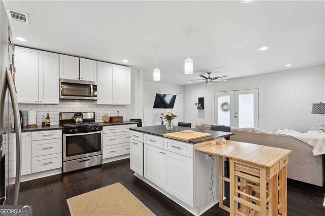 kitchen with dark wood-type flooring, backsplash, dark countertops, appliances with stainless steel finishes, and white cabinets