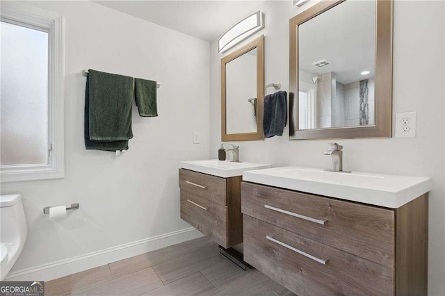 full bath with toilet, two vanities, baseboards, and a sink