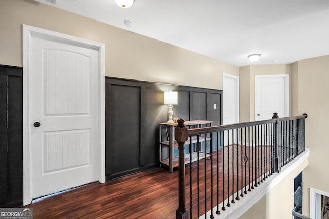 corridor with a wainscoted wall, an upstairs landing, dark wood-style flooring, and a decorative wall