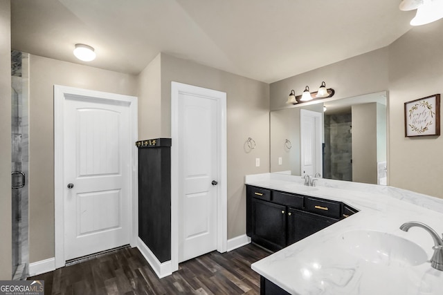 bathroom with a shower stall, baseboards, double vanity, wood finished floors, and a sink