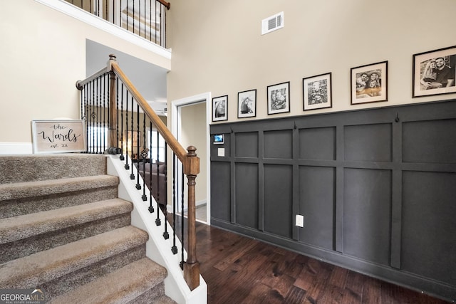 stairs featuring a decorative wall, wood finished floors, visible vents, and a towering ceiling