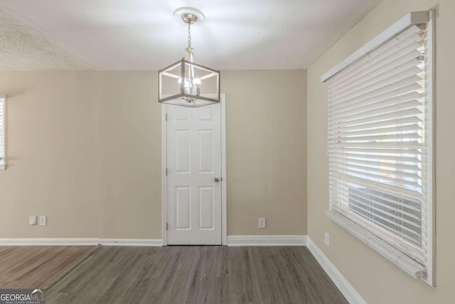 unfurnished dining area with a notable chandelier, wood finished floors, and baseboards