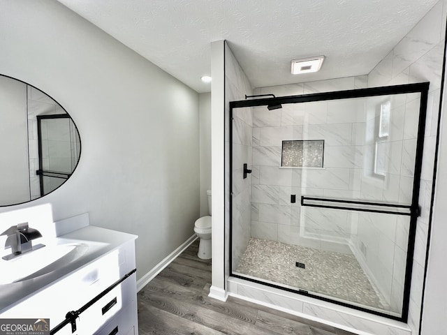 full bath with toilet, a textured ceiling, wood finished floors, a shower stall, and vanity