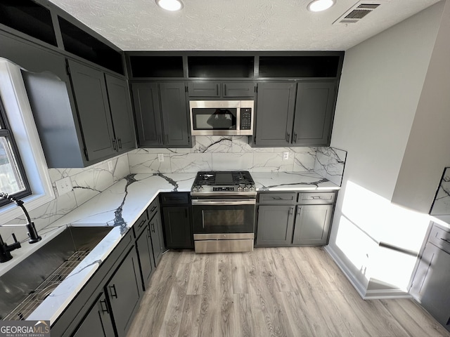 kitchen featuring light stone countertops, visible vents, light wood finished floors, a sink, and appliances with stainless steel finishes