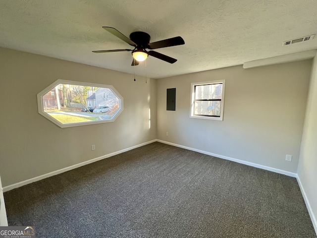 spare room featuring dark carpet, electric panel, visible vents, and a wealth of natural light