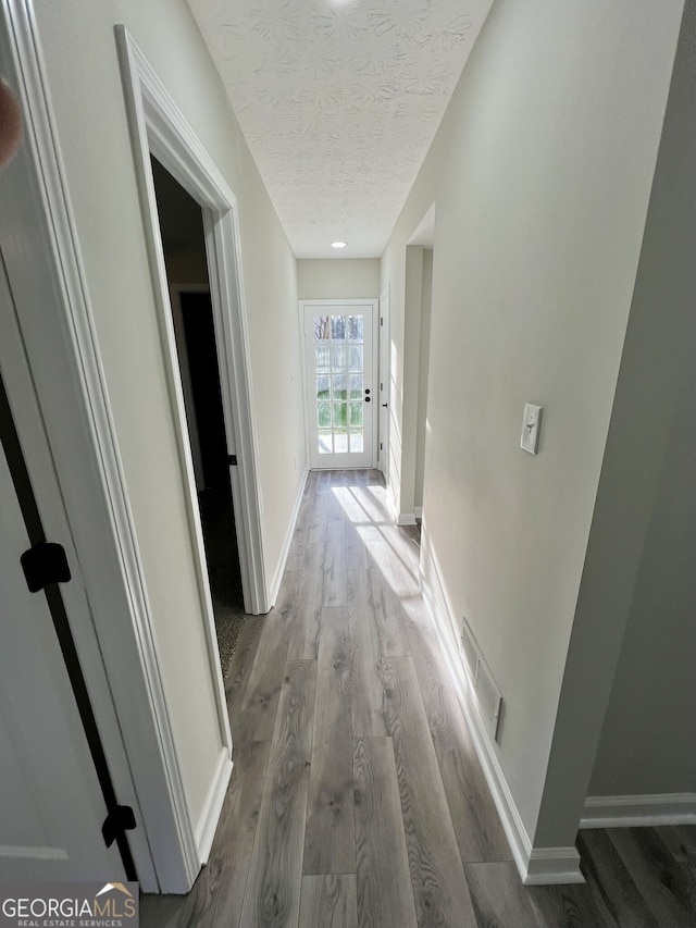 hall featuring visible vents, baseboards, a textured ceiling, and wood finished floors