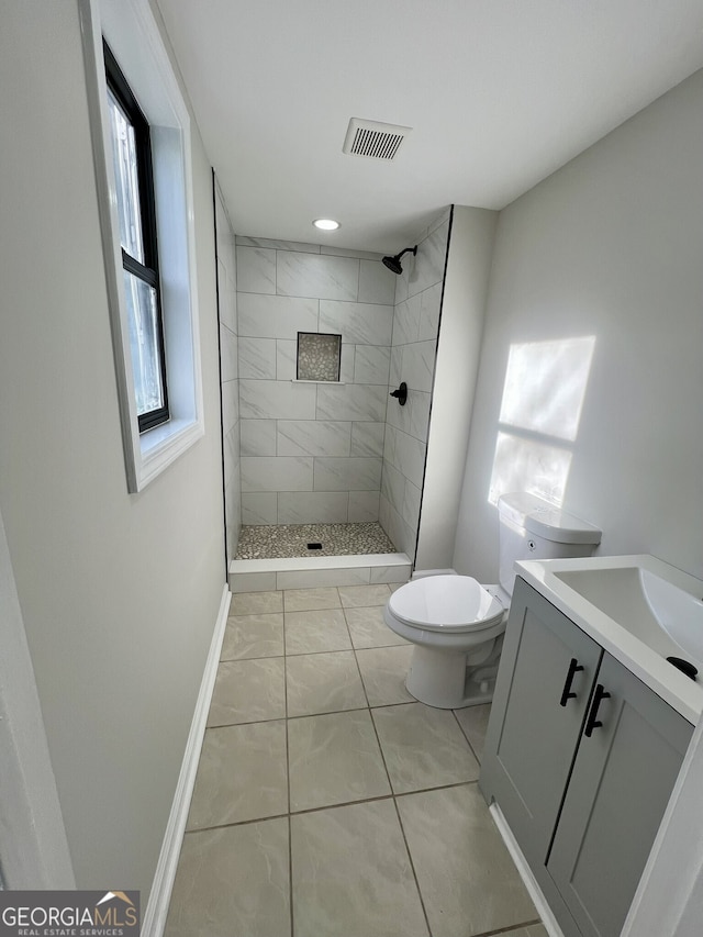 bathroom featuring visible vents, toilet, baseboards, tiled shower, and vanity