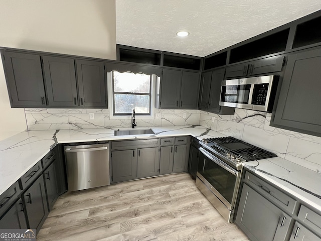 kitchen with light stone counters, a sink, stainless steel appliances, light wood-style floors, and a textured ceiling