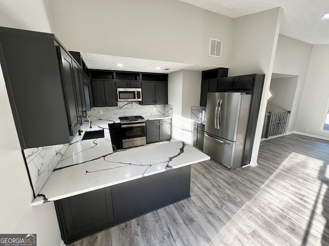 kitchen featuring visible vents, light wood finished floors, high vaulted ceiling, a peninsula, and appliances with stainless steel finishes