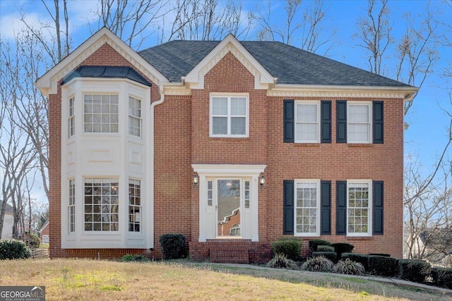 view of front facade featuring brick siding, roof with shingles, and a front lawn