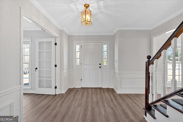 foyer featuring stairs, wood finished floors, a wainscoted wall, and ornamental molding