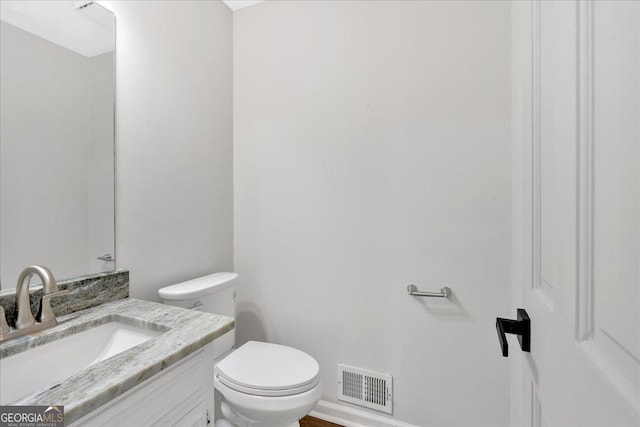 half bath with visible vents, toilet, and vanity