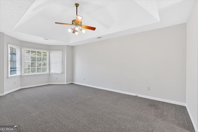 spare room featuring dark carpet, baseboards, a tray ceiling, and a ceiling fan