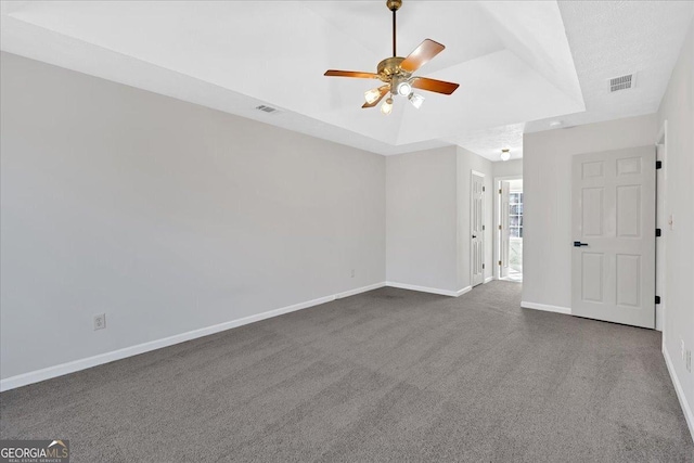 carpeted empty room with visible vents, a ceiling fan, a raised ceiling, and baseboards