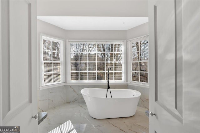 bathroom with marble finish floor and a freestanding bath