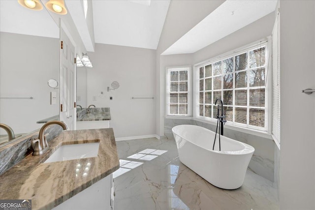 bathroom with baseboards, vaulted ceiling, a freestanding tub, marble finish floor, and vanity