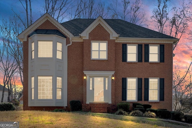 view of front of home featuring brick siding, a shingled roof, and a yard