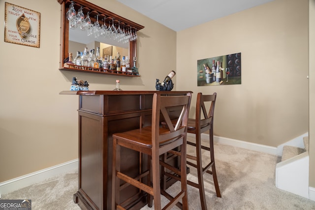 bar featuring baseboards, a bar, stairs, and carpet