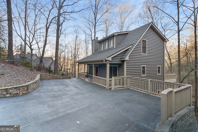 view of side of home featuring a chimney, a porch, and a shingled roof