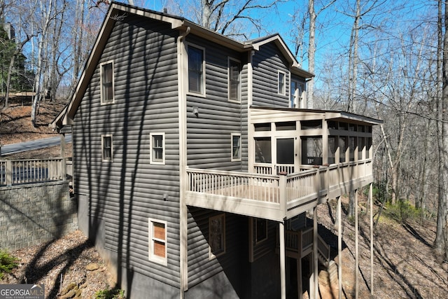 view of home's exterior featuring a deck, log veneer siding, and a sunroom