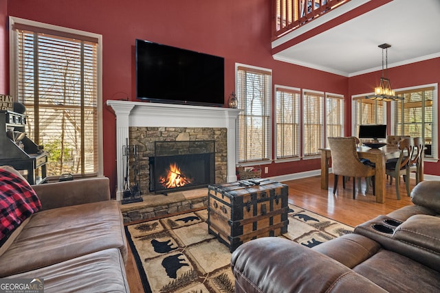 living area featuring baseboards, ornamental molding, a stone fireplace, an inviting chandelier, and wood finished floors