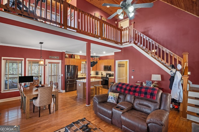 living area featuring light wood-type flooring, a ceiling fan, stairway, a high ceiling, and baseboards