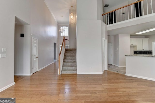 unfurnished living room with baseboards, a chandelier, a towering ceiling, and light wood finished floors