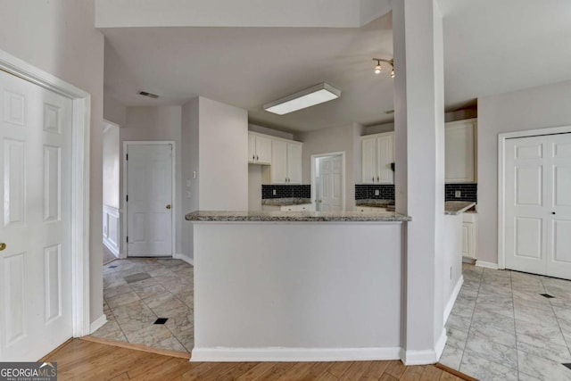 kitchen featuring tasteful backsplash, visible vents, baseboards, light stone counters, and white cabinets