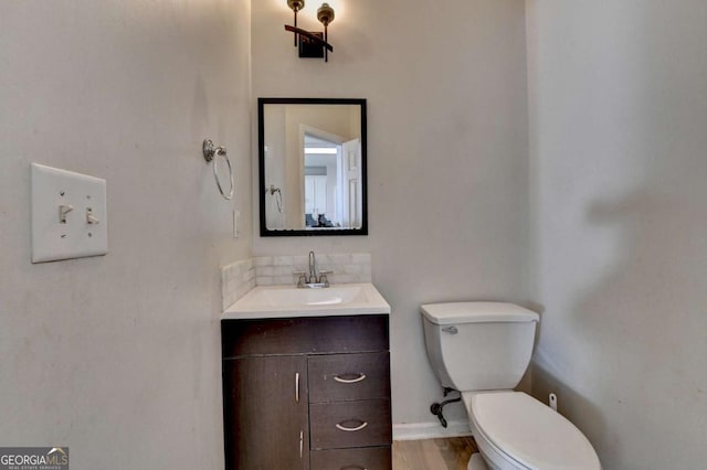 half bathroom with baseboards, toilet, wood finished floors, and vanity