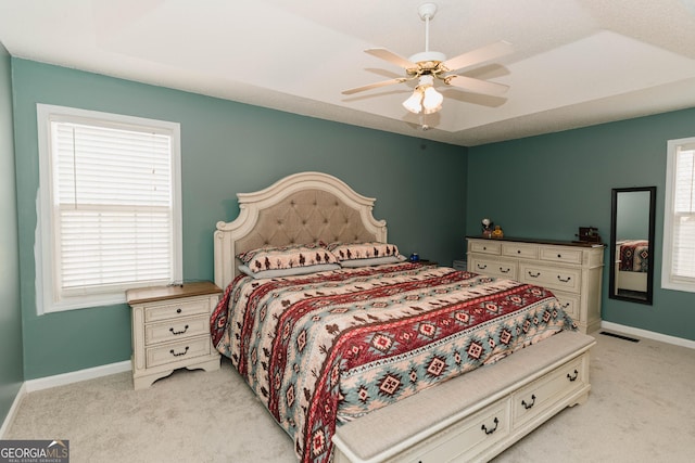 bedroom featuring light colored carpet, a raised ceiling, and multiple windows