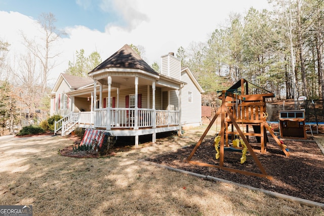 rear view of property with covered porch, a chimney, a playground, and a trampoline