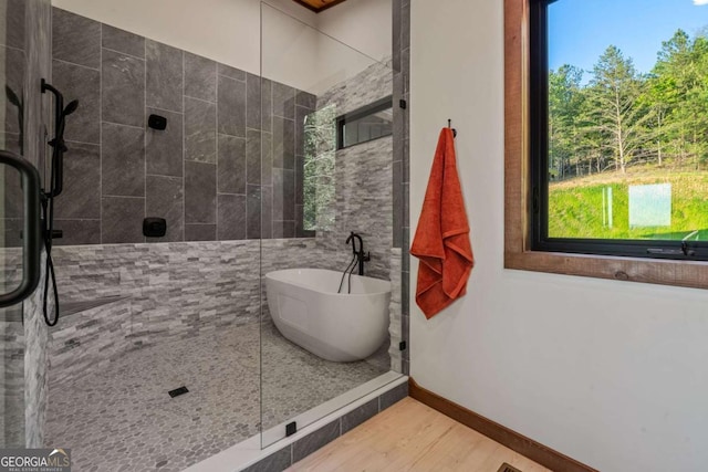 bathroom with baseboards, tiled shower, a soaking tub, and wood finished floors