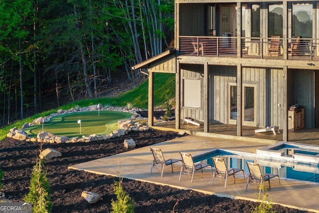 rear view of house with board and batten siding, a balcony, a patio area, an outdoor pool, and an in ground hot tub