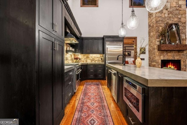 kitchen with light countertops, built in appliances, pendant lighting, light wood-type flooring, and backsplash