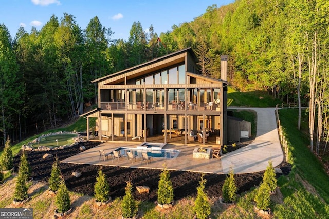 back of house with a chimney, a hot tub, a patio, and a view of trees