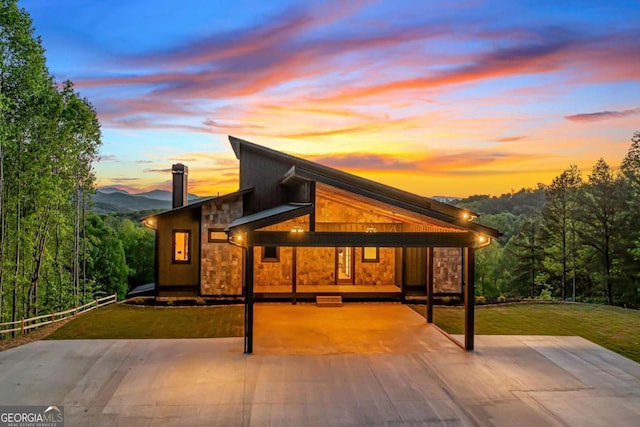 back of property at dusk with a yard and stone siding