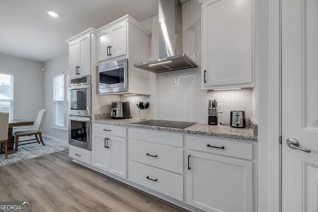 kitchen with tasteful backsplash, white cabinets, appliances with stainless steel finishes, and wall chimney exhaust hood