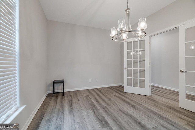 unfurnished dining area featuring a notable chandelier, baseboards, and wood finished floors