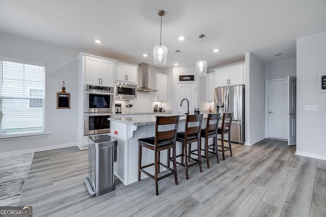 kitchen featuring a center island with sink, white cabinets, stainless steel appliances, and wall chimney exhaust hood