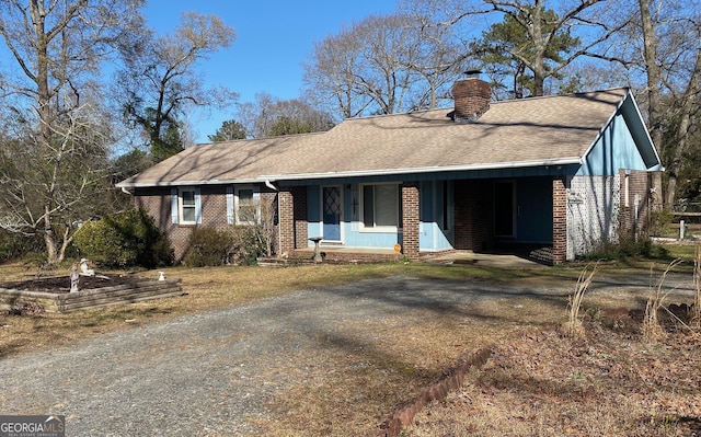 ranch-style home featuring a shingled roof, brick siding, driveway, and a chimney