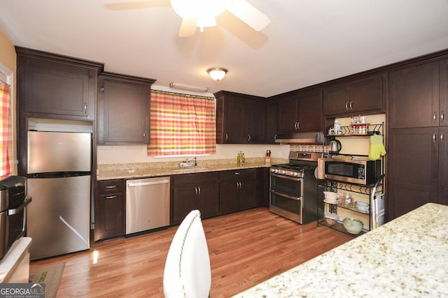 kitchen featuring light wood finished floors, a sink, dark brown cabinets, under cabinet range hood, and appliances with stainless steel finishes