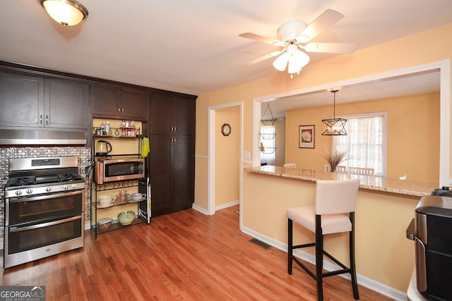 kitchen featuring visible vents, under cabinet range hood, appliances with stainless steel finishes, a kitchen breakfast bar, and light wood-type flooring