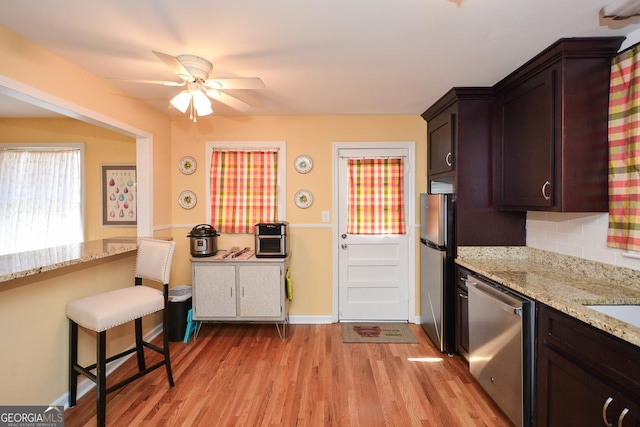 kitchen with light stone counters, stainless steel appliances, decorative backsplash, dark brown cabinetry, and light wood-style floors