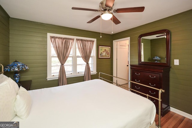 bedroom with wood walls, ceiling fan, and wood finished floors