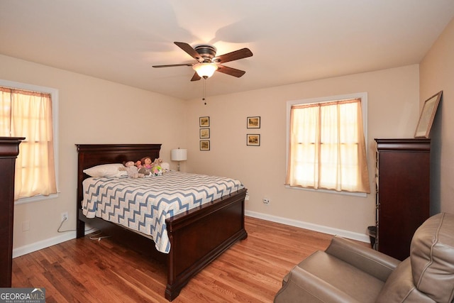 bedroom featuring ceiling fan, baseboards, multiple windows, and wood finished floors