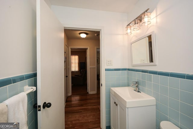 half bathroom with vanity, tile walls, wood finished floors, and a wainscoted wall