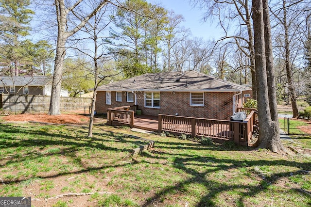 rear view of house with brick siding, a wooden deck, a yard, and fence