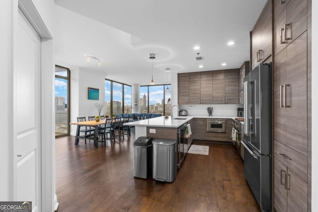 kitchen featuring a peninsula, high end fridge, light countertops, dark wood-type flooring, and expansive windows