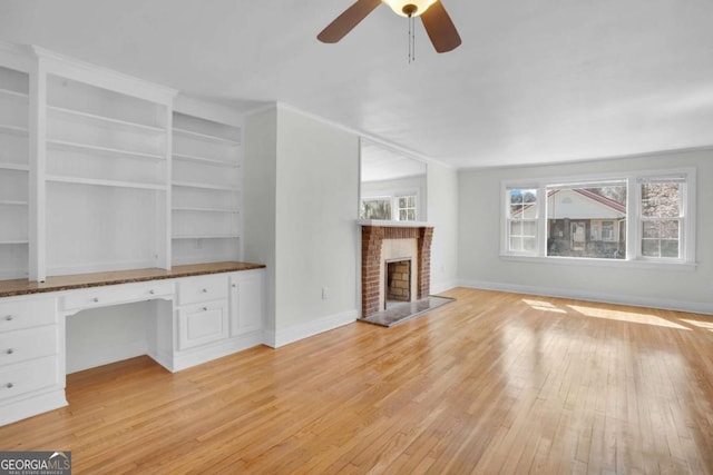 unfurnished living room with a brick fireplace, built in study area, light wood-type flooring, and baseboards