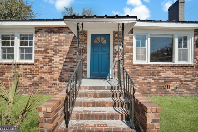 view of exterior entry featuring brick siding and a chimney